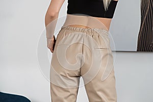 Stylish beautiful young blond woman in a tight biege pants, black top and white shirt near a white wall in the room. Attractive