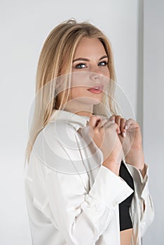 Stylish beautiful young blond woman in a tight black pants, black top and white shirt near a white wall in the room. Attractive