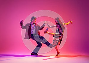 Stylish, beautiful young couple, man and woman in retro clothes dancing swing against pink background in neon light