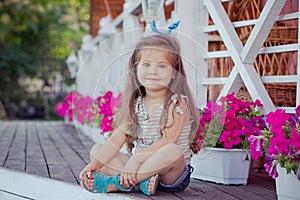 Stylish beautifull cute baby girl with brunette hair posing on wooden garden full of flowers wearing tiny jeans shirts and airy sk