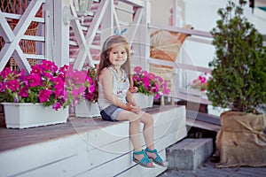 Stylish beautifull cute baby girl with brunette hair posing on wooden garden full of flowers wearing tiny jeans shirts and airy sk photo