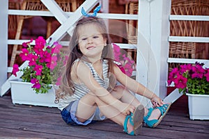 Stylish beautifull cute baby girl with brunette hair posing on wooden garden full of flowers wearing tiny jeans shirts and airy sk