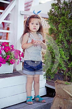Stylish beautifull cute baby girl with brunette hair posing on wooden garden full of flowers wearing tiny jeans shirts and airy sk photo