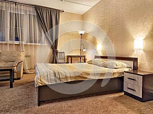 Stylish bedroom in beige tones and colors with double bed, sofa and table. Concept of cozy bedroom, living room or hotel