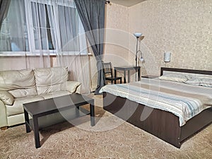 Stylish bedroom in beige tones and colors with double bed, sofa and table. Concept of cozy bedroom, living room or hotel