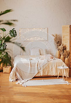 Stylish bedroom in bright boho style. A cozy modern interior with an abundance of textiles and living indoor plants