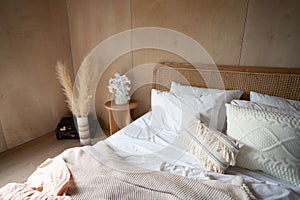 Stylish Bedroom corner with rattan headboard and bed with soft pillows setting with white pillows plywood wall on the background