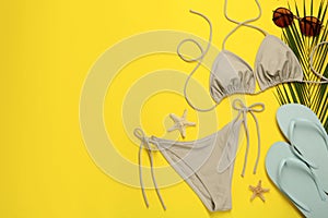 Stylish beige bikini and beach accessories on yellow background, flat lay. Space for text