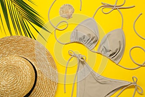 Stylish beige bikini, hat and seashell on yellow background, flat lay