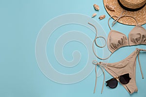 Stylish beige bikini, sunglasses and hat on light blue background, flat lay. Space for text