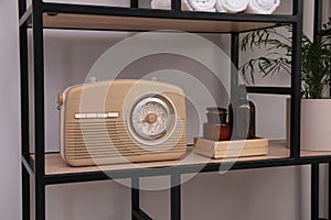 Stylish beige radio on rack with toiletries and houseplant indoors