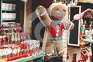 Stylish big christmas gingerbread man toy at wooden houses with candy canes in holiday winter fair. Christmas festive street decor