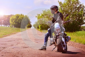 Stylish biker with motorbike stoped on a abandoned road. Motorcycle background. Tonned.