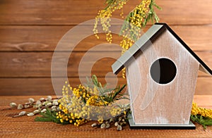 Stylish bird house and fresh flowers on wooden table. Space for text
