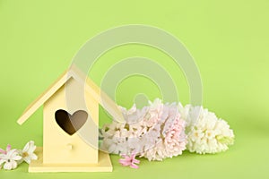 Stylish bird house and fresh hyacinths on green background. Space for text
