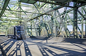 Stylish black big rig semi truck with covered black semi trailer running with cargo on the truss bascule Columbia River Interstate
