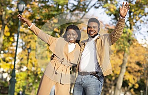 Stylish black couple posing with raised hands in autumn park