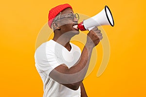 Stylish black handsome smiling american man in white t-shirt speaks news through a megaphone on isolated orange