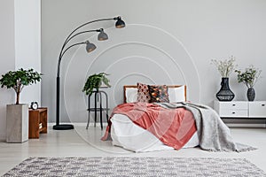 Stylish black lamp green plant bed with pillows and blanket and white bedside table in modern bedroom
