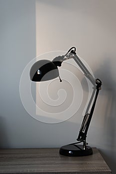 Stylish black lamp from Ikea on the wooden table with sun reflect on the background