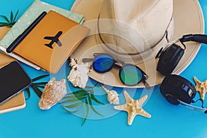 stylish black phone, passport, sunglasses, map, hat, headphones, shells, notebook on trendy blue paper. flat lay. planning summer