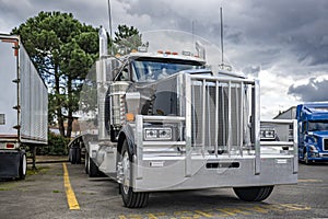 Stylish black powerful big rig semi truck tractor with huge grille guard and empty flat bed semi trailer standing on the truck