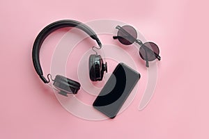 stylish black sunglasses,smartphone and headphones on pink background, flat lay. modern hipster image. black items on pink paper.