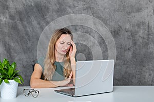 Stylish Blond Woman in Gray Dress Posing Next to Laptop and Green Flower