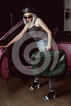 stylish blonde woman in beret and sunglasses opening vintage car and holding