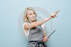 Stylish blonde woman hairdresser aiming with sissors to a side over blue photo