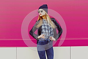 Stylish blonde woman model wearing black rock style clothes over a pink background