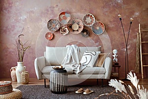 The stylish boho compostion at living room interior with design beige sofa, coffee table, wicker baskets and elegant personal