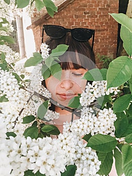 Stylish boho girl taking selfie with white flowers on green branches of bird-cherry tree. Girl portrait with beautiful bird cherry