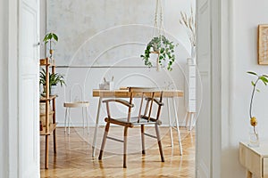 Stylish and boho home interior of open space with wooden desk, chair, lamp and white shelf. Design and elegant personal.