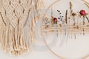 Stylish boho wreath with dry flowers and macrame hanging on white wall. Modern floral arrangement and creative handmade decor in