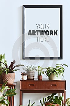 Stylish botany composition of home garden interior with wooden mock up poster frame, filled a lot of beautiful house plants.