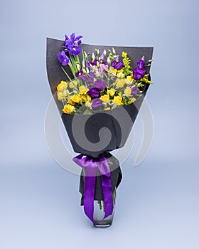 Stylish bouquet of yellow and purple flowers wrapped in black paper on a blue background.