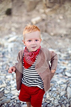 Stylish boy child in a vest stands on a pebble beach