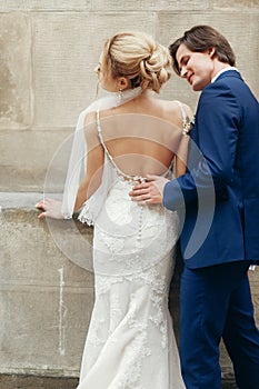 Stylish bride back and groom embracing in city street. happy luxury wedding couple hugging at old building in light. romantic