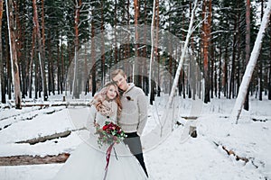 Stylish bride and groom with a bouquet are posing on background of the snowy forest. Winter wedding.