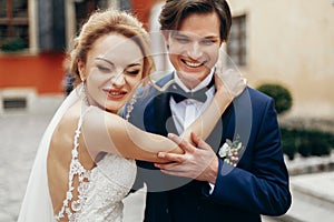 Stylish bride and groom dancing and embracing in city street. happy luxury wedding couple hugging at old building in light.