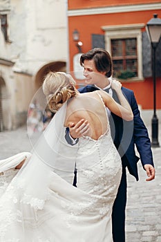 Stylish bride and groom dancing and embracing in city street. happy luxury wedding couple hugging at old building in light.