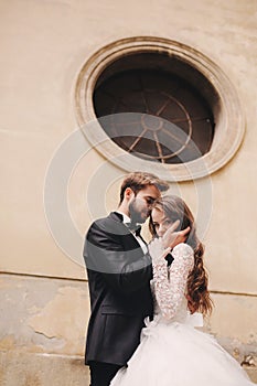 Stylish bride and groom gently hugging in european city street. Gorgeous wedding couple of newlyweds embracing near ancient