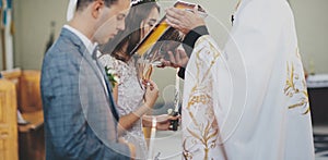 Stylish bride and groom kissing holy bible from priest hands during matrimony in church. Wedding ceremony in cathedral. Classic photo