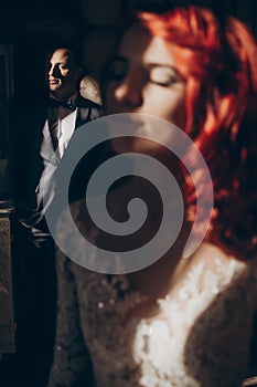 Stylish bride and groom posing in light and shadow, creative photo, on background of wooden wall in country. rustic wedding