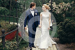 Stylish bride and groom relaxing in park.  happy luxury wedding couple walking and smiling among trees. man in blue suit and woman