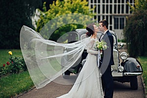 stylish bride and groom sensually posing near retro car with boh
