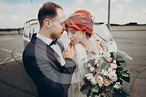 Stylish bride and groom sensually posing near retro car with boho bouquet. luxury wedding couple newlyweds embracing. space for