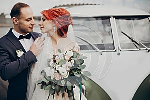 Stylish bride and groom sensually posing near retro car with boho bouquet. luxury wedding couple newlyweds embracing. space for