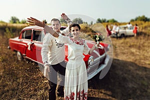 Stylish bride and happy groom near car on the background of nature and friends bridesmaids